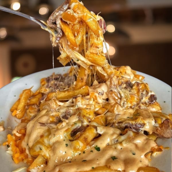 A fork lifts cheesy fries with meat from a plate, showing melted cheese strings.