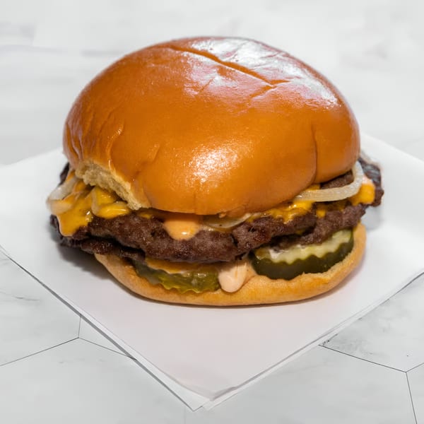A WattaBun double smash burger with melted cheese, onions, pickles, and special sauce on a brioche bun.