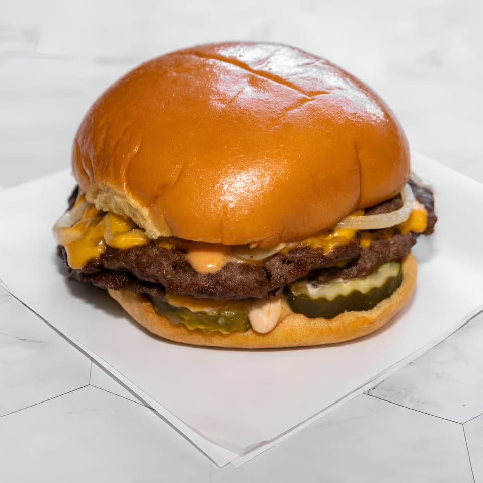 A WattaBun double smash burger with melted cheese, onions, pickles, and special sauce on a brioche bun.