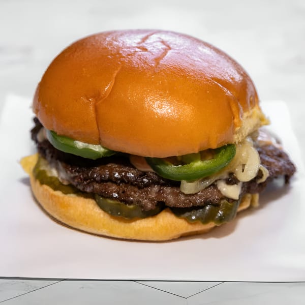 A WattaBun double smash burger with melted cheese, grilled onions, jalapeños, and pickles.